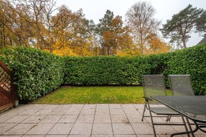 A patio with a metal table and chairs, a hedge, and a grassy area.