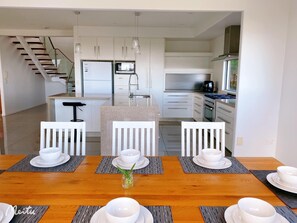 Una cocina moderna con armarios blancos, horno empotrado y zona de comedor con mesa de madera preparada para cuatro comensales.