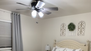 Ein Schlafzimmer mit Bett, Deckenventilator, Fenster mit Jalousien und dekorativer Wandgestaltung.