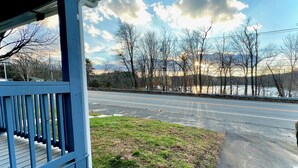 A view from a porch overlooking a road with a body of water and mountains in the distance.