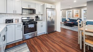 A modern kitchen with stainless steel appliances, white cabinetry, and hardwood flooring.