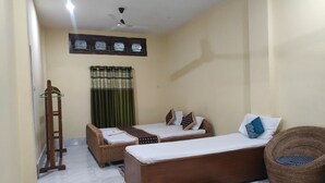 Una habitación con dos camas individuales, un sofá, una silla de mimbre, un ventilador de techo y una ventana con cortinas.