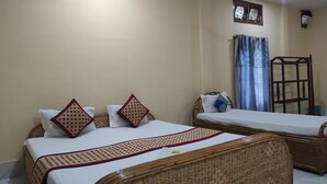 Una habitación con dos camas individuales, un cabecero de madera, un ventanal pequeño con cortinas y una silla de madera.