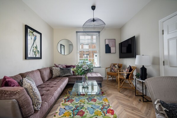 A living room with a sofa, a coffee table, a chair, a TV, and a window with blinds.