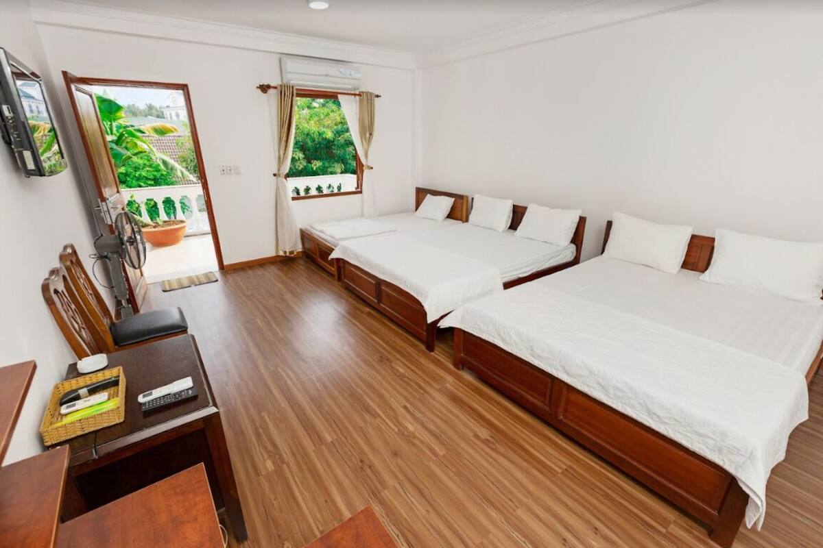 A hotel room with two single beds, a wooden desk with a chair, a TV, and a window with curtains.