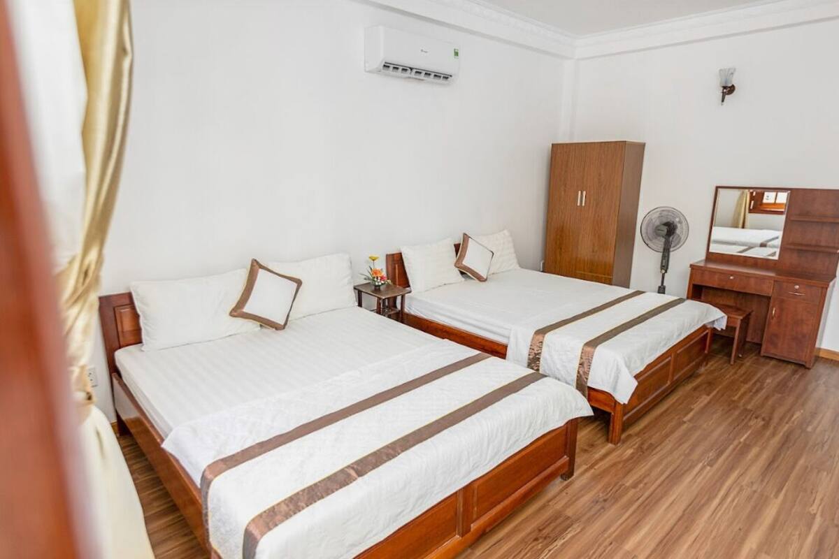 A hotel room with two single beds, a wooden wardrobe, a desk with a mirror, and a standing fan.
