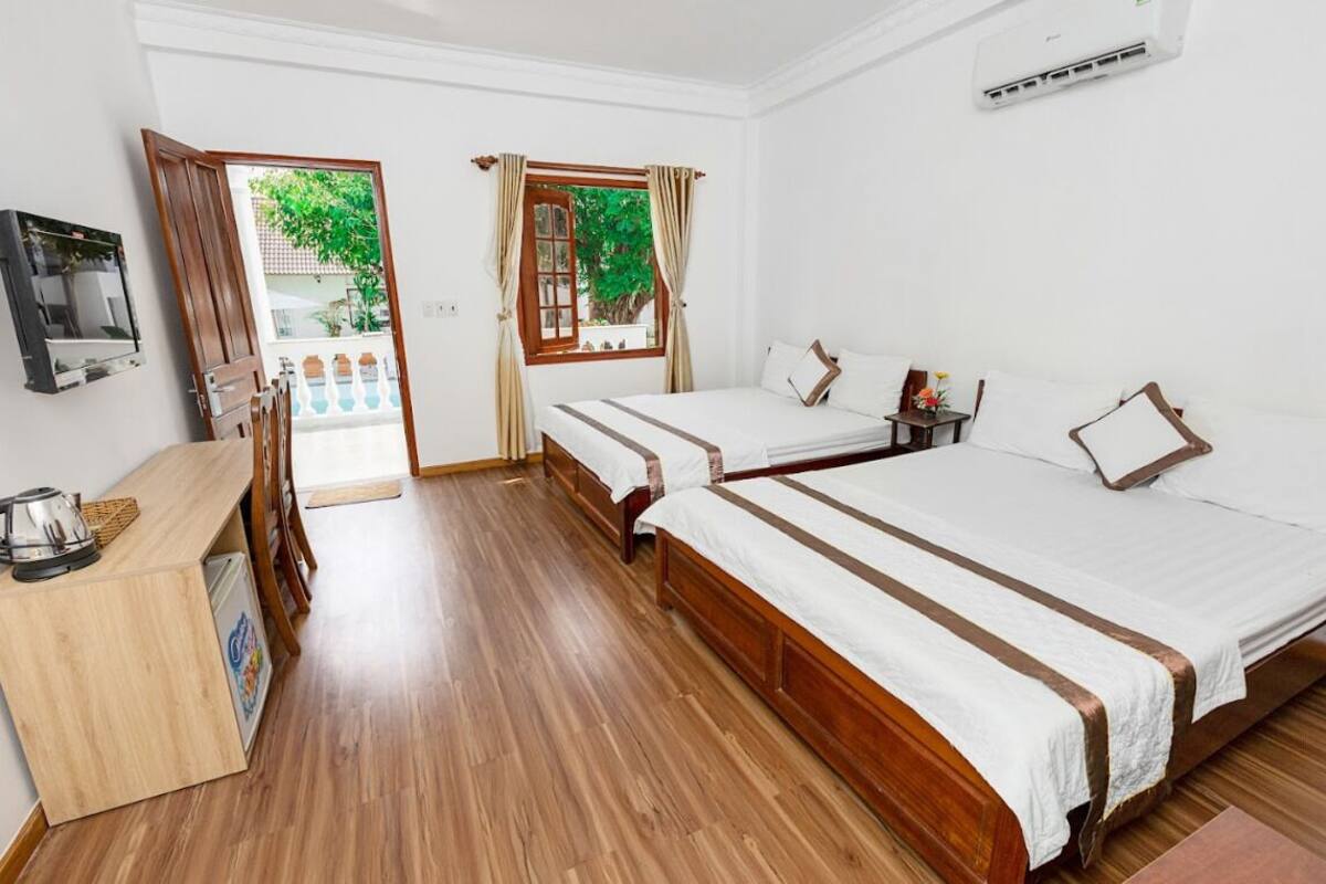A hotel room with two beds, a wooden floor, a TV, a small table, and a window with curtains.