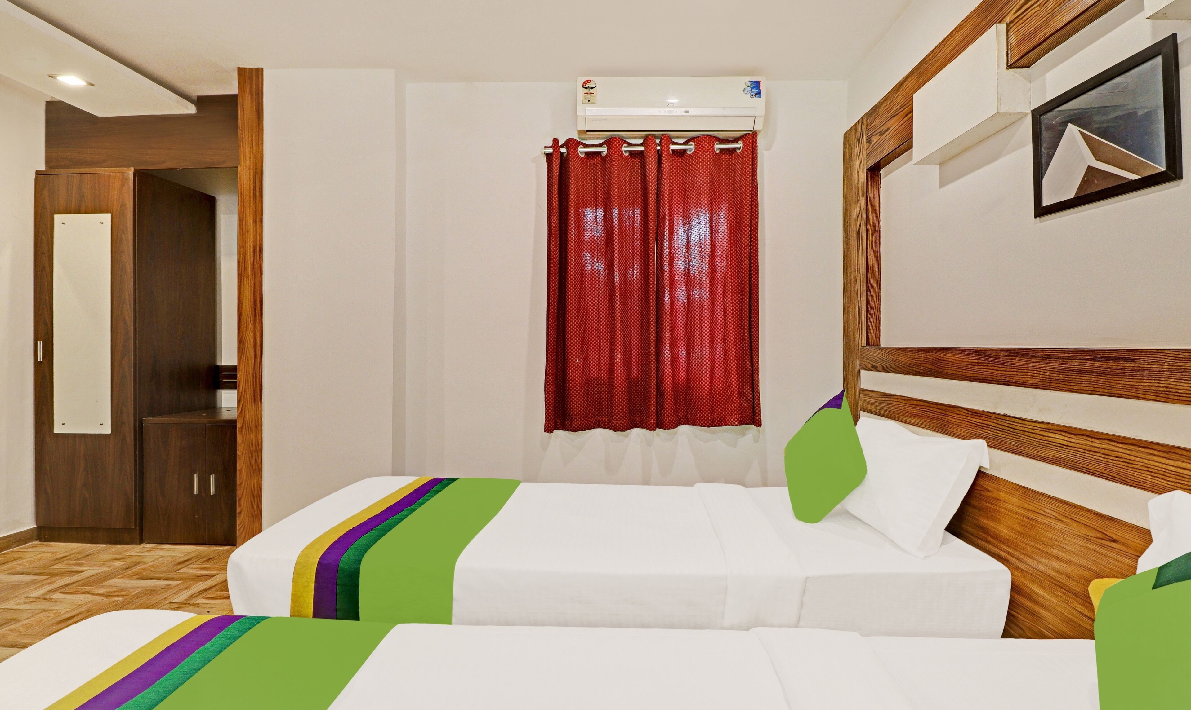 Habitación de hotel con cama, cabecera de madera, cortina roja y aire acondicionado de pared.
