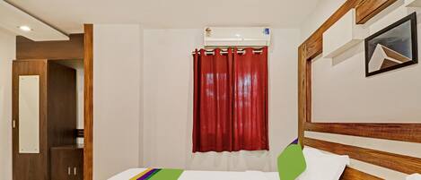 Habitación de hotel con cama, cabecera de madera, cortina roja y aire acondicionado de pared.
