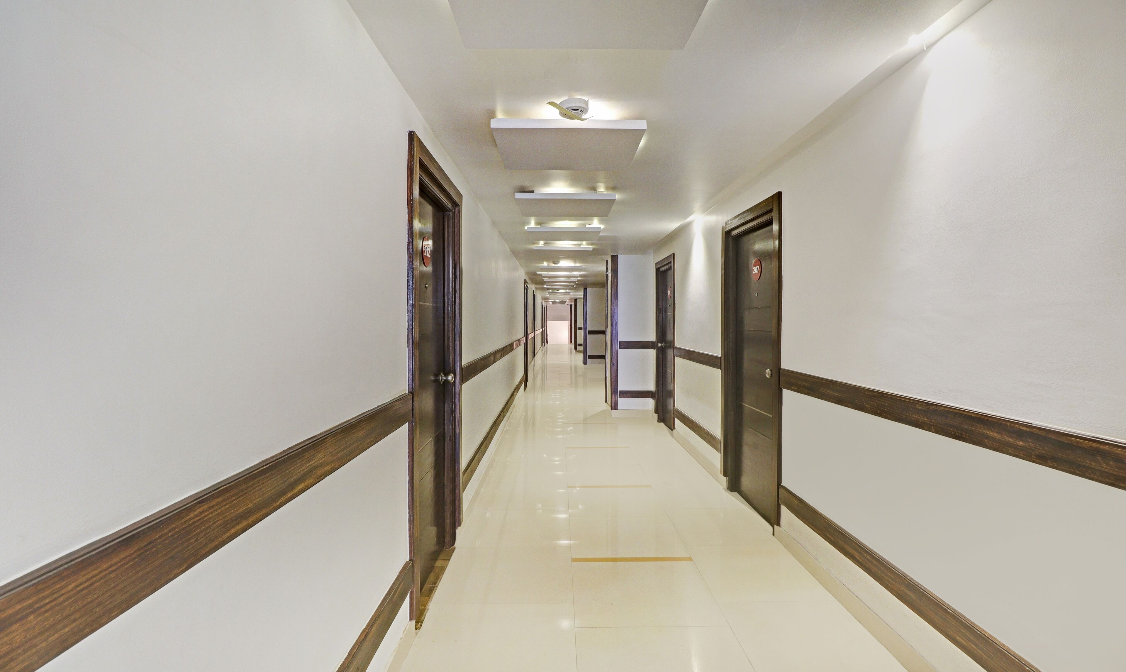A long, well-lit hallway with doors on both sides, leading to rooms.
