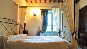 A bedroom with a bed, a nightstand, a lamp, a chair, and a window with curtains. - MACETONA - MACETONA-SUITE (San Casciano dei Bagni)