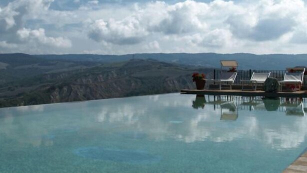 A clear pool with lounge chairs and a potted plant, overlooking a mountainous landscape. - MACETONA - MACETONA-SUITE (San Casciano dei Bagni)
