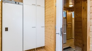 Un interior de madera con un armario blanco, una puerta que da a una cocina y un tapete a rayas.