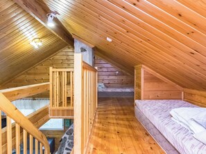 A wooden interior with a sloped ceiling, a bed with white bedding, and a staircase leading to an upper level. - Pyhä-vuonelo by Interhome (Pelkosenniemi)