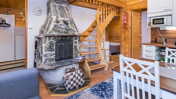 Interior acogedor de una cabaña con chimenea de piedra, escalera de madera y kitchenette.