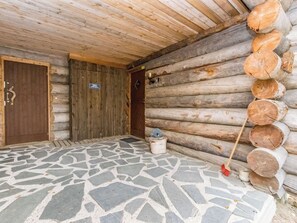 A log cabin with a stone-tiled entrance, a wooden door, and a stack of logs against the wall.
