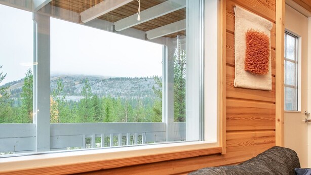 L’intérieur d’une cabane, avec une grande fenêtre donnant sur une montagne boisée.