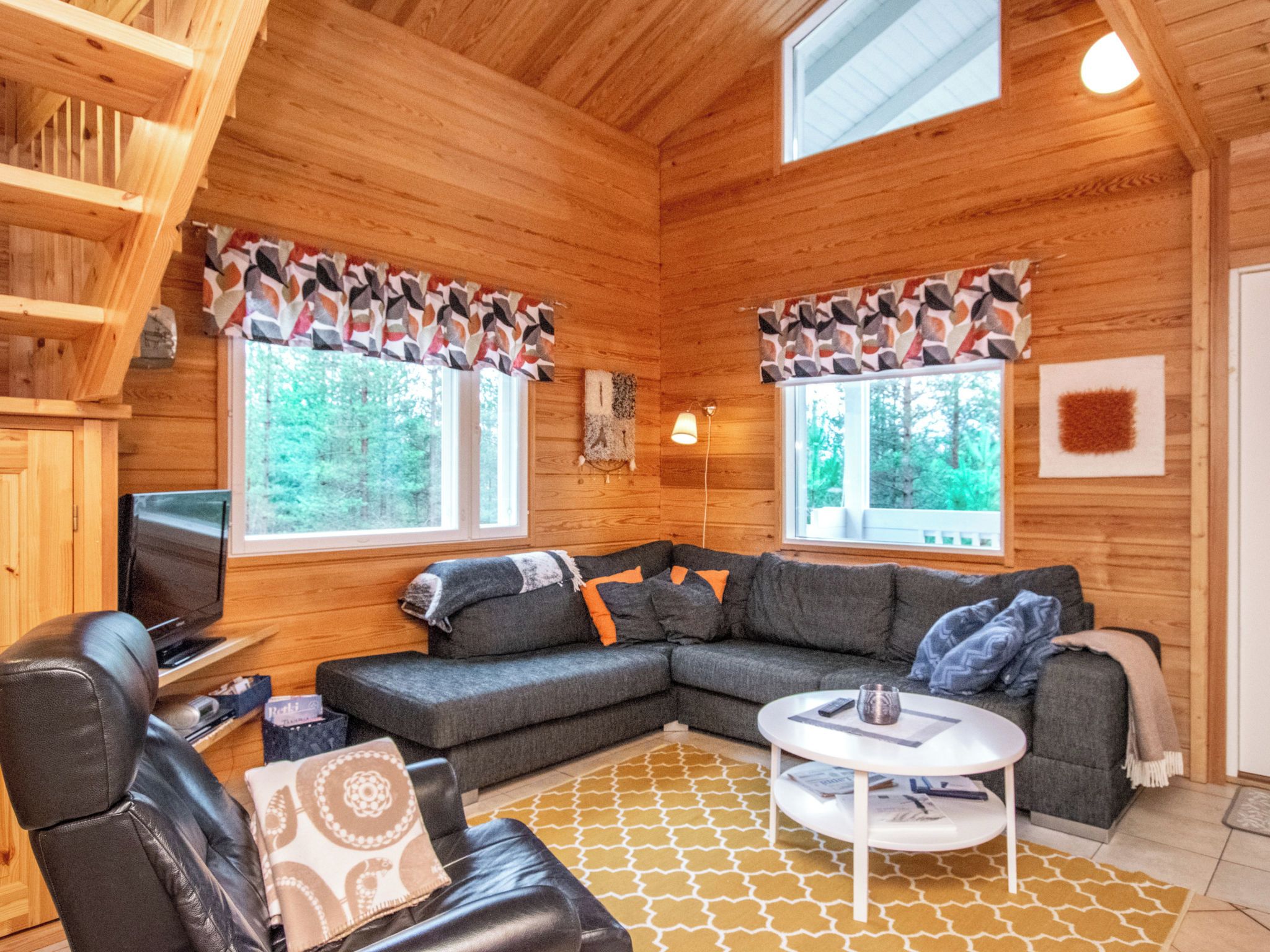 Un intérieur de chalet chaleureux avec un canapé d’angle, un fauteuil en cuir, un téléviseur et une petite table.