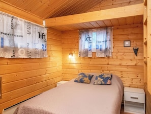 Une chambre de cabane en bois comprenant un lit, deux oreillers, une table de chevet et un luminaire fixé au mur.