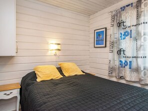 Een slaapkamer met een bed, twee kussens, een nachtkastje, een wandlamp, een lijst met een afbeelding en een gordijn met tekst.