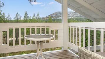 A wooden deck with a table and wicker chair, overlooking a forested landscape.