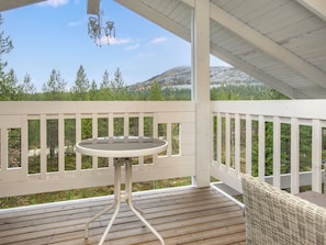 Une terrasse en bois avec une table et une chaise en osier, donnant sur un paysage boisé.