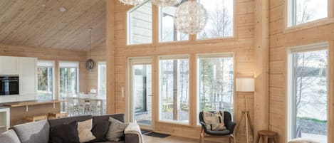 A spacious living room with a sofa, coffee table, and a chair. There are large windows and a view of the outdoors.