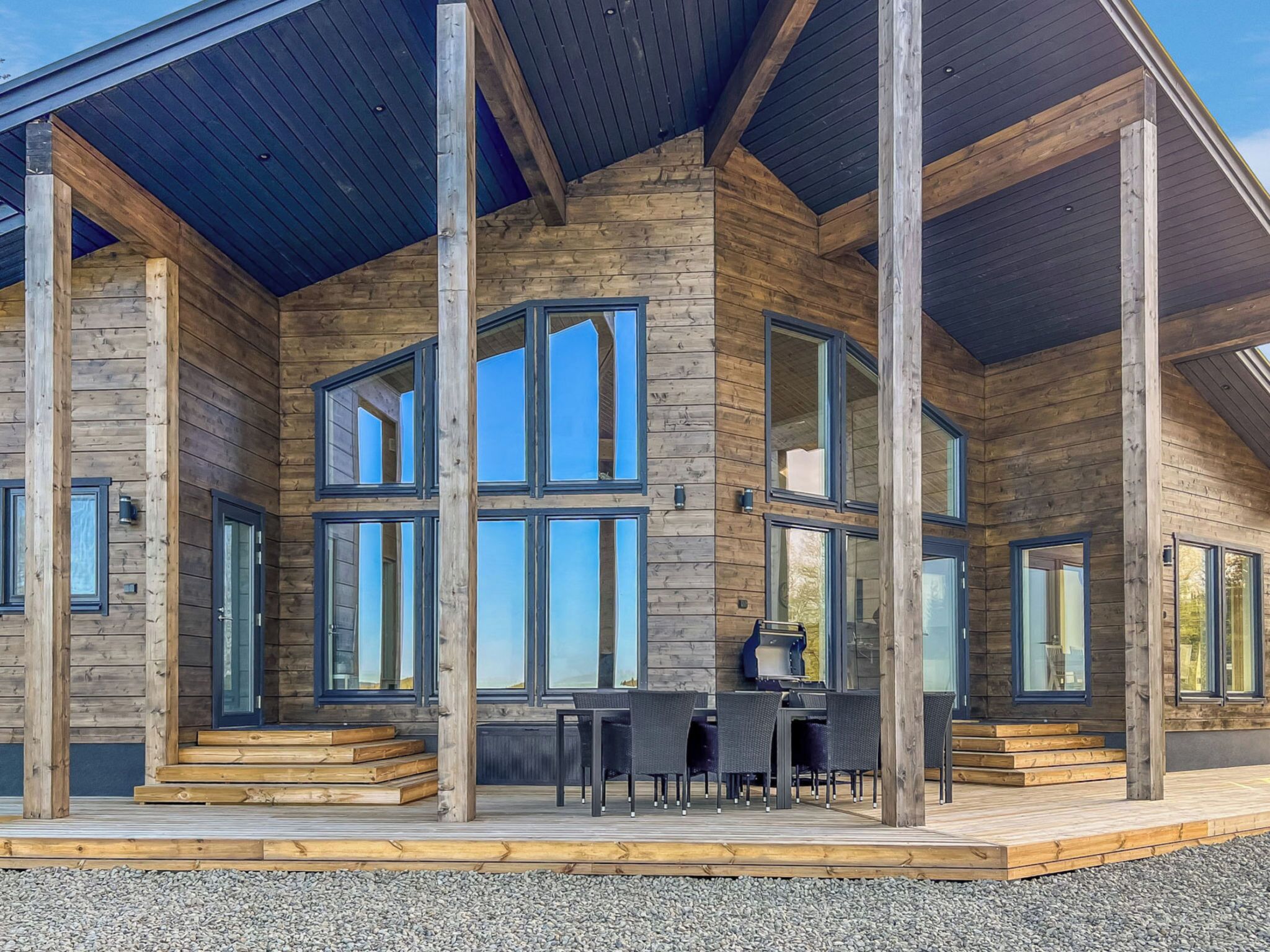 En moderne hytte med store vinduer, en overdækket terrasse og en pejs af sten.