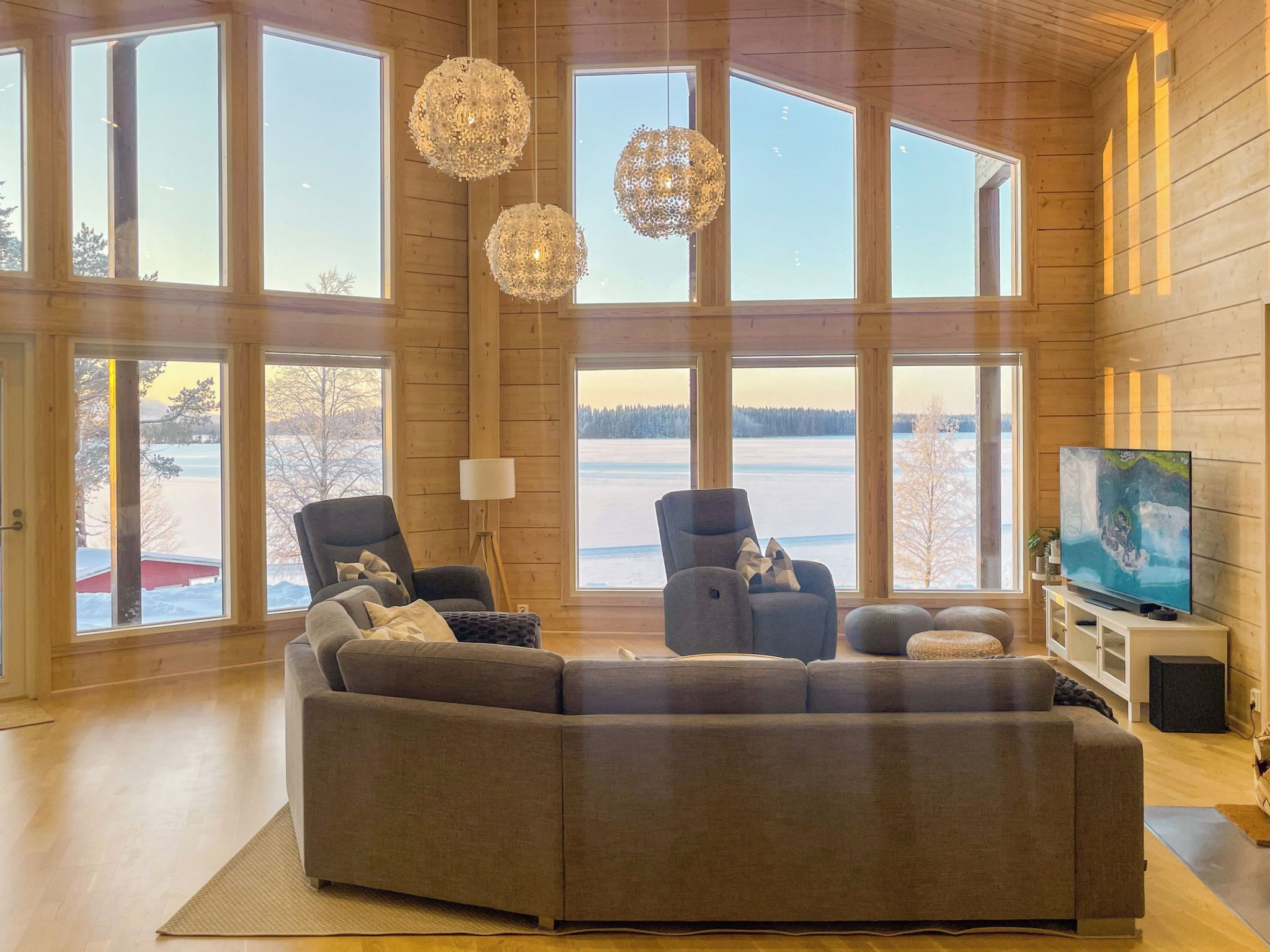 A spacious living room with large windows, a sectional sofa, two armchairs, and a television on a stand.
