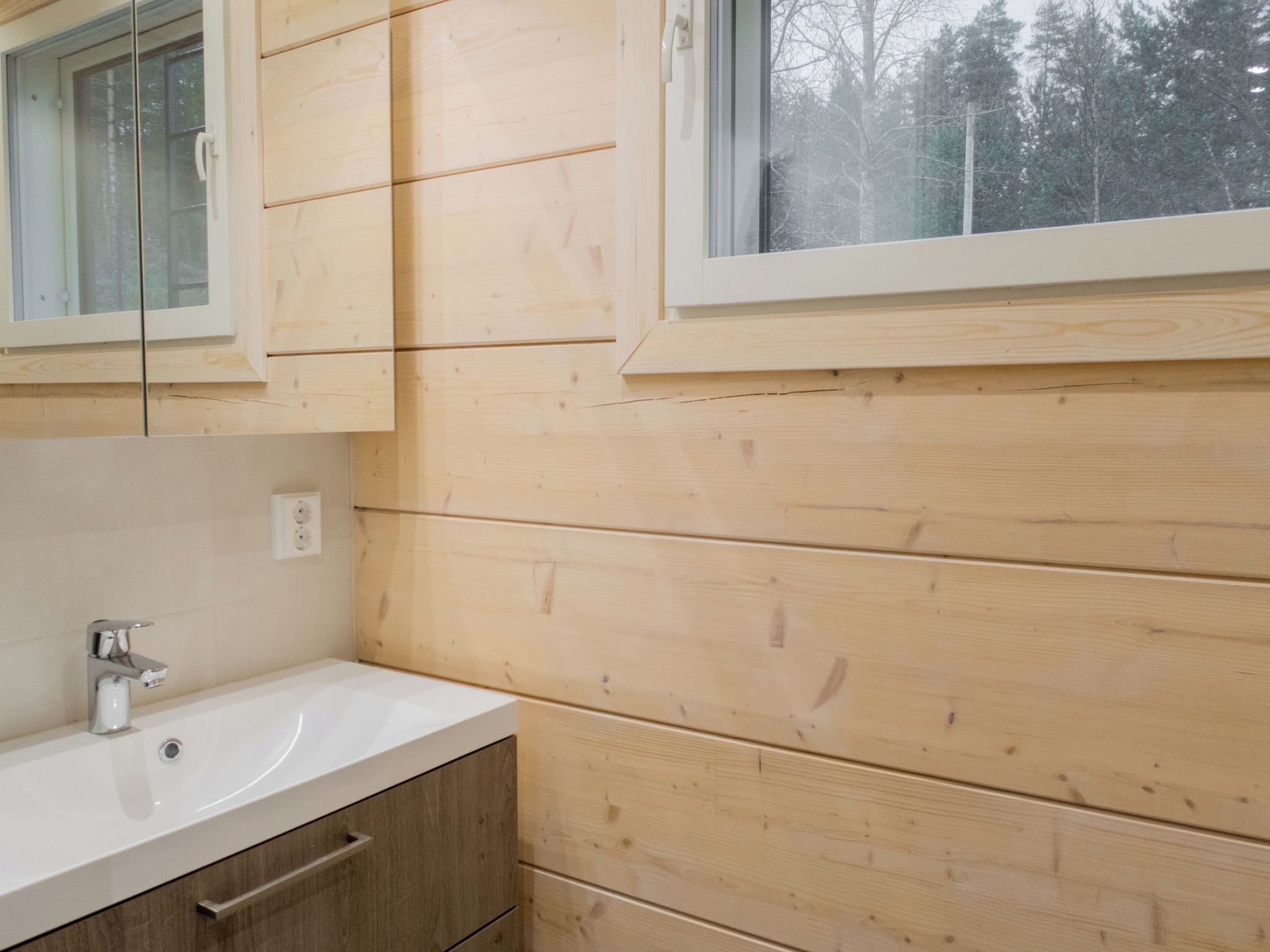 A bathroom with wooden walls, a white sink, and a window.