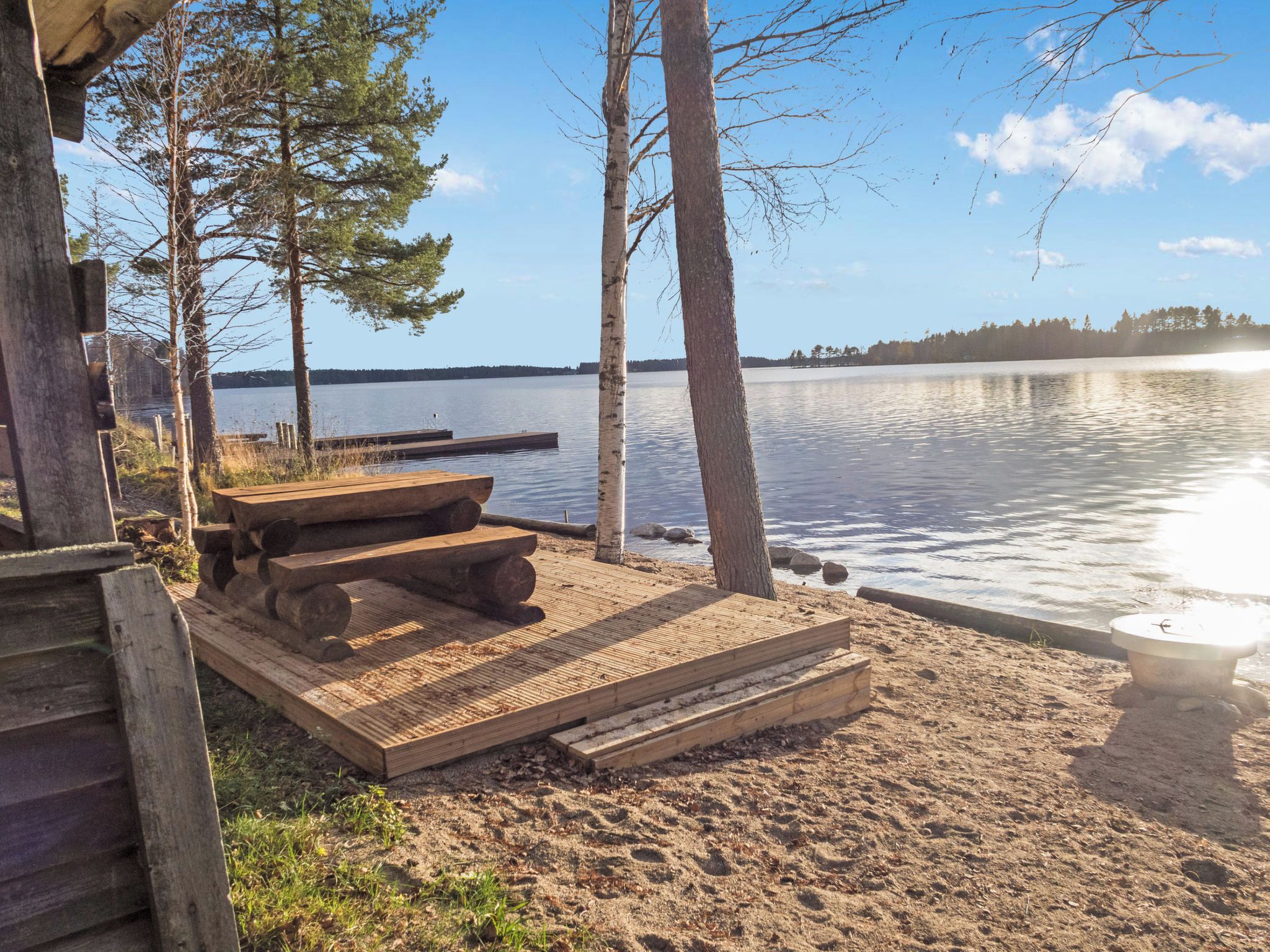 Eine Holzterrasse mit Picknicktisch und Bänken mit Blick auf einen ruhigen See und Steg.