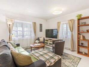 Een woonkamer met een bank, fauteuils, een salontafel, een televisie en een boekenkast.