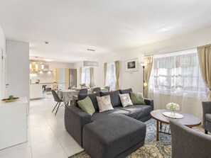 A modern living room with a grey sectional sofa, a dining area with a table and chairs, and a kitchen in the background.