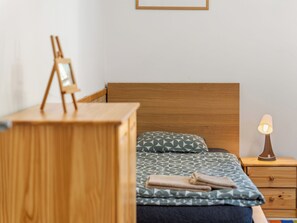 Ein ordentlich eingerichtetes Schlafzimmer mit einem hölzernen Kopfteil, einem Nachttisch mit Lampe und einem Bett mit gemusterten Betttextilien.