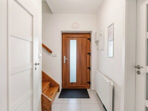 Een gang met een houten deur, een witte radiator en een zwarte mat.
