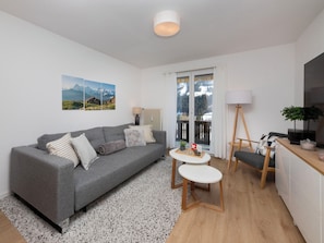 Uma sala de estar moderna com um sofá cinzento, uma mesinha redonda e uma cadeira de madeira.
