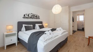 A neatly made bed with a grey headboard, white bedding, and a grey blanket. There are two bedside tables with lamps, a wall art piece, and a hanging light fixture. - Chalet zur Höhe by Interhome (Grindelwald)