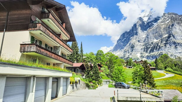 A multi-story building with balconies, a parking area, and a mountain backdrop. - Chalet zur Höhe by Interhome (Grindelwald)