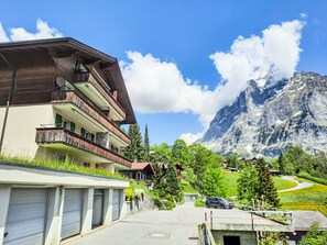 Un edificio de varios pisos con balcones, un estacionamiento y montañas al fondo.