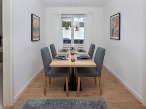 Un comedor con una mesa de madera dispuesta para cuatro personas, sillas tapizadas de gris y cuadros en las paredes.