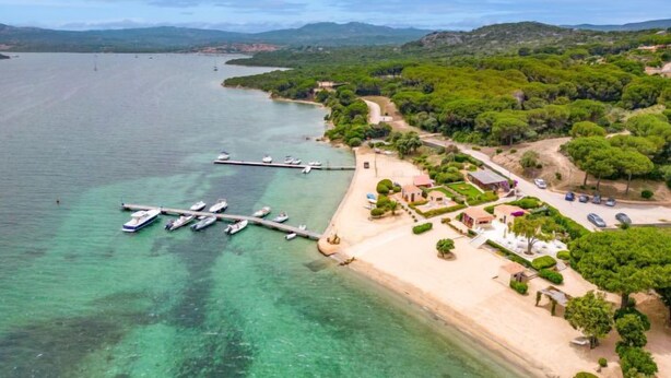 An aerial view of a coastal area with a marina, sandy beach, and lush greenery.