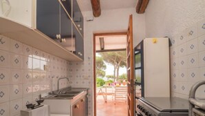 A compact kitchen with a sink, stove, and refrigerator. A window leads to an outdoor patio area.