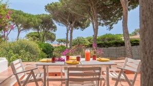 An outdoor dining area with a table set for four, surrounded by trees and a view of the sea.