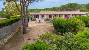 A villa with a tiled roof, a covered patio, and a garden with various plants and a tree.