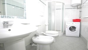 Un baño con lavamanos, inodoro, bidé, ducha y lavadora.