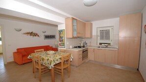 Una cocina compacta con armarios de madera, una mesa de comedor con sillas, un sofá y un ventanal con cortinas.