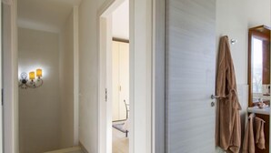 Un couloir avec un luminaire, une porte donnant sur une salle de bain et un peignoir accroché au mur.