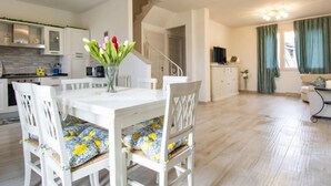 Une cuisine moderne avec des meubles blancs, un coin repas avec une table et des chaises blanches, et un escalier menant à un autre niveau.