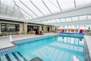 An indoor swimming pool with a glass ceiling, stone pillars, and a tiled edge. - Luxury Farm House With Swimming Pool Eurovision 23 (St Helens)