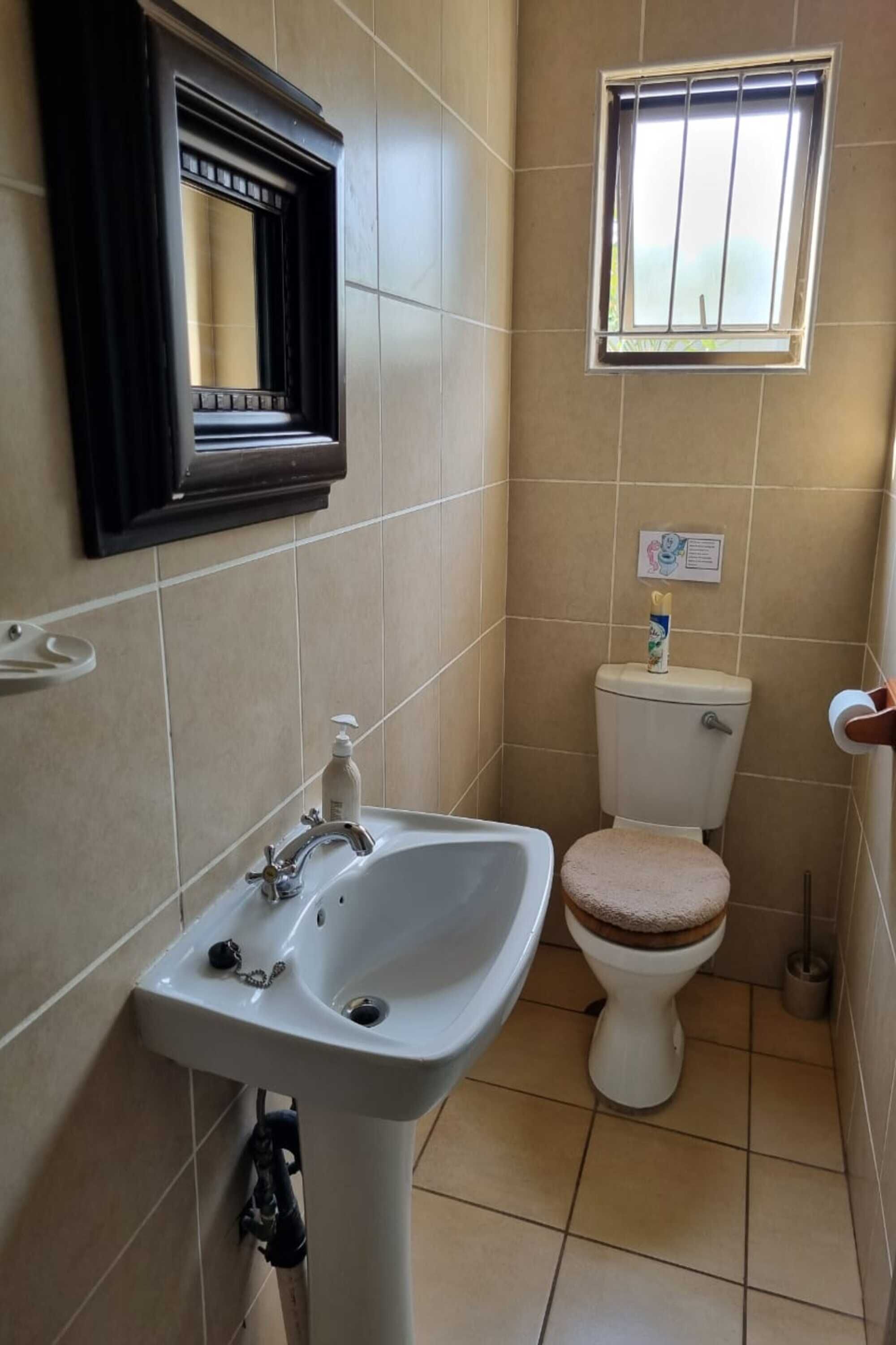 A bathroom with a white sink, a toilet, and a window with bars.
